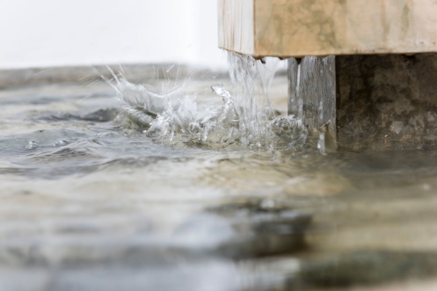 Quellwasser läuft aus einem Holzrohr in ein Becken aus Naturstein im Haus