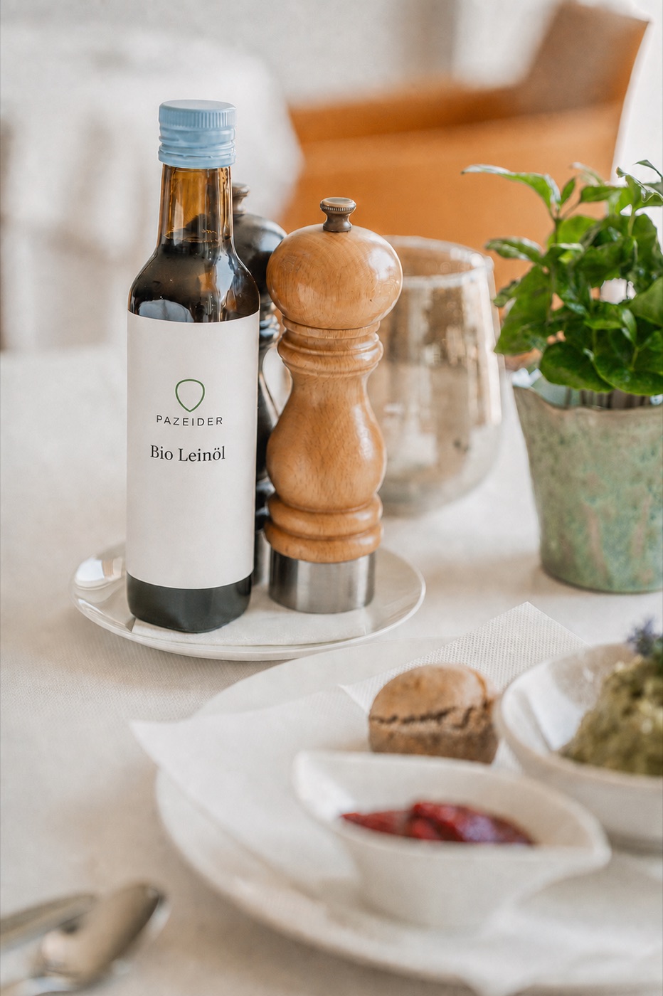Flasche Bio Leinöl mit dem Zeichen des Hauses auf einem gedeckten Tisch, daneben Pfeffermühle und Brot